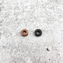 Two small, flat washers—one copper-colored, one black—from the Messermeister Custom Mod Kit Handle Hardware are placed side by side on a textured gray surface, ideal for upgrading your next knife handle with quality Messermeister hardware.