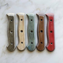 Five Messermeister Custom Russet Mod Kit Handles - Large are displayed on a light marble surface in gray, beige, green, brown, and red, each featuring three holes for attaching to the blade.