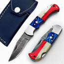 Two Texan Knives Lone Star 3-Inch Damascus Pocket Knives—custom handmade with bone and Pakka wood handles—one open and one closed, are shown beside a dark blue leather sheath with white stitching.