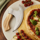A round pizza is partially sliced with the Custom Handmade Ax Pizza Cutter by Texan Knives, featuring an 8" J2 steel blade and hand-engraved ash wood handle. Cherry tomatoes and basil leaves accent this unique kitchen tool.