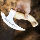 A hand holds the Texan Knives Custom Hand Engraved Ax Pizza Cutter, featuring an 8-inch curved J2 steel blade engraved with ancient runic symbols and a wooden handle, set against a blurred earthy-toned background.
