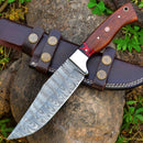 The Texan Knives Custom Handmade Damascus Skinning Blade – 4.5" Damascus Steel with a wooden handle rests on a brown leather sheath, displayed against tree bark and green leaves.