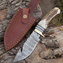 The Texan Knives Custom Handmade Damascus Steel Guthook Skinning Knife features a 9" patterned blade, stag horn handle with brass guard, and comes with a brown leather sheath.