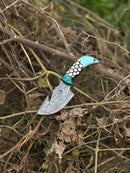 The Texan Knives Custom Handmade Damascus Steel Guthook Skinning Knife features a striking turquoise, black, and white resin handle and patterned 7.5” blade, making it an appealing decorative hunting knife. Includes a leather sheath.