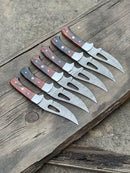 Six Texan Knives Custom Handmade Damascus Steel Hunting Blades with 4-inch resin handles are neatly arranged on a weathered wooden surface, highlighting detailed designs and expert craftsmanship from the Texan Knives brand.