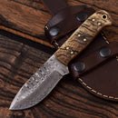 The Texan Knives Custom Handmade Damascus Steel Skinning Knife features a 4.5" patterned blade and a textured sheep horn handle, resting on a brown leather sheath with black metal rivets on a rustic wooden surface.