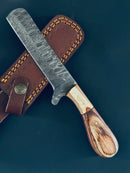 The Cowboy Bull Cutter Knife by Texan Knives features a 5" Damascus steel blade and Pakkawood handle, resting on a brown leather sheath with yellow stitching and button closure—ideal for collectors of handmade or cowboy bull cutter knives.