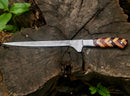 The Texan Knives Handmade Damascus Fillet Knife 8” with a patterned blade and a rosewood & olive wood handle, complete with leather sheath, lies on a tree stump amid greenery.