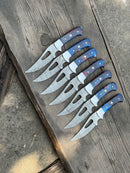 Seven Texan Knives Custom Handmade Good Hunting Knives, each with a 4" Damascus steel blade and blue and red handles, are arranged in a fan shape on weathered wood with concrete around it.
