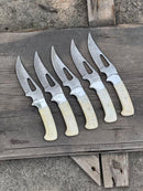 Five Texan Knives Custom Hunting Knives—handmade Damascus steel blades and light handles—are lined up outdoors on a weathered wood surface.