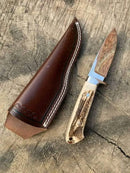 The Texan Knives Custom Handmade Knife Belt features a J2 steel blade and stag horn handle, paired with a leather sheath, displayed on a weathered wooden surface.