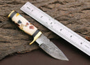 The Texan Knives Custom Handmade Damascus Steel Outdoor Knife by Texan Knives features a 3" blade and a handle adorned with colored stones. Measuring about 5" long, it’s shown beside a metal ruler on a rugged wooden surface.