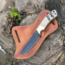 The Texan Knives Custom Handmade Rasp Tool Knife with Sheep Horn Handle rests on a brown leather sheath atop a textured tree stump near a green plant—perfect ranch outdoor gear for enthusiasts.