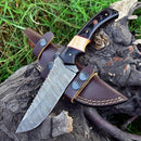 Experience precision and craftsmanship with our Custom Handmade Skinning Blades from Texan Knives—a large, ornate Damascus steel knife with a wooden handle rests on a brown leather sheath, perfect for any hunting enthusiast.