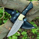 A Texan Knives Custom Handmade Skinning Knife featuring a Damascus steel blade and a black Buffalo Horn & Camel Bone handle sits on a tree branch, partially sheathed in a black leather case with white stitching. Green foliage appears in the background.