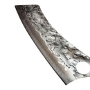 A close-up of the Spaceman Knives Meteor Series Mega Chef knife, featuring a hammered finish and a round tip hole, rests on light marble beside a dark cloth.