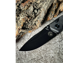 The Spaceman Knives N1 EDC, featuring a textured Micarta handle and 14C28N Sandvik steel blade with an etched logo, rests on rough gray stone beside tree bark.