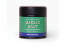 A 3.1 oz (88g) jar of World Spice Garlic Salt by World Spice, made with California garlic and Italian sea salt, featuring a green and blue label with the words “Umami • Salty • Herbal” and topped with a black lid.