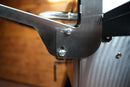 Close-up of a Pimp My Grill® Tactical Stainless Folding Front Shelf attached to a Camp Chef Woodwind 24 with two silver screws.
