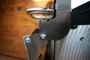 Close-up of a stainless steel hinge bracket for a Pimp My Grill® Tactical Stainless Folding Front Shelf attached to the side of a Camp Chef Woodwind 24 / Woodwind Pro 24 / CL 24 grill.