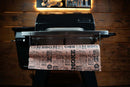 Pimp My Grill Tactical Stainless Folding Front Shelf attached to a Camp Chef Woodwind 24 / Woodwind Pro 24 / CL 24, with a sheet of printed butcher paper draped over the grill prep workspace.