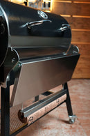 A Pimp My Grill® Tactical Stainless Folding Front Shelf attached to a black Recteq Patio Legend 410, with a roll of butcher paper suspended underneath for added grill prep space.
