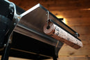 Pimp My Grill® Tactical Stainless Folding Front Shelf attached to a Recteq Patio Legend 410 grill, featuring a hook holding a roll of butcher paper for added prep space.