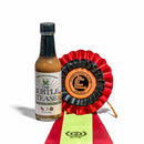 A bottle of California Hot Sauce Solutions CHSS The Subtle Tease Hot Sauce sits beside a black-and-red ribbon showcasing an International Flavor Awards medallion, with a green and red ribbon beneath it.