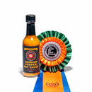 A bottle of California Hot Sauce Solutions Paulman Acre Smoked Pepper Hot Sauce, an award-winning all-purpose hot sauce from California Hot Sauce Solutions, stands beside a colorful orange, green, and blue International Flavor Awards ribbon on a white background.