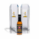 A bottle of California Hot Sauce Solutions Paulman Acre Smoked Pepper Hot Sauce, renowned for its all-purpose versatility, is displayed in front of two crystal Sparky Awards trophies labeled 2023 Grand Champion and Smoked Style Winner.