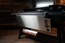 Stainless steel Pimp My Grill® Tactical Stainless Folding Front Shelf for Traeger Ironwood XL attached to a pellet grill, featuring a paper towel roll holder mounted underneath to maximize prep space.