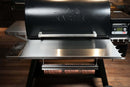 Pimp My Grill® Tactical Stainless Folding Front Shelf for Traeger Timberline 1300 attached to a black pellet grill, featuring a built-in towel rack holding a roll of butcher paper to expand your outdoor grill workspace.