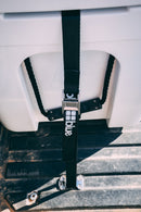 A Blue Coolers Secure Universal Tie Down Kit with a black strap and metal buckle secures a white cooler to a truck bed.