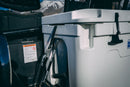 A white cooler secured in the bed of a vehicle using a Blue Coolers Secure Universal Tie Down Kit For Adventurers, featuring two black nylon straps with metal buckles.