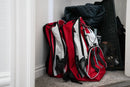 Two red and white Blue Seventy Two Ultimate Tactical 3 Day Emergency Kit For Preppers leaning against a wall on a carpeted floor.