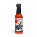 A glass bottle of California Hot Sauce Solutions J's Small Batch The OG Hot Sauce features a bold red sauce made with the fiery kick of Chile de Árbol. The label, set against a white background, displays an illustrated blue classic car and reads "Small Batch Hot Sauce," while also highlighting "No sugar - No preservatives.
