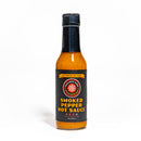 A bottle of California Hot Sauce Solutions Paulman Acre Smoked Pepper Hot Sauce, featuring an orange-yellow sauce inside, a black label, and a black cap, set against a plain white background.
