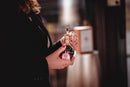A person with red nail polish holds a small bottle of Taycte Acetaia Malpighi D.O.P. Traditional Balsamic Vinegar of Modena — Affinato Grade, Aged 12+ Years, featuring a gold seal and red label, while standing outdoors.