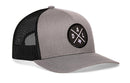The Haka Hat Dallas Trucker Hat in gray and black features a mesh back, snapback closure, and a front patch with crossed lines, "DAL X" letters, and the outline of Texas.