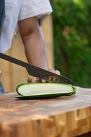 Dalstrong Shadow Black Carving Set – Titanium BBQ Knife and Fork Set for Slicing and Serving shown with a cucumber and slicing it