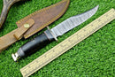 The Texan Knives Western Boulder Colorado Knife, featuring an 11" handmade Damascus steel blade with an epoxy resin handle and brass guard, is displayed beside a wooden ruler and brown leather sheath on green artificial grass.