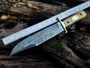 The Texan Knives Damascus Steel Cowboy Bowie Knife – 13" features a patterned blade, brass guard, and camel bone handle. It rests diagonally on weathered wood, with a metallic ruler above showing its impressive 8-inch blade length. Leather sheath included.