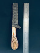 A Texan Knives Cowboy Bull Cutter Knife with a 5" Damascus steel blade and pakkawood handle rests beside a metal ruler on a dark surface.