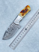 The Texan Knives Damascus Steel Fixed Blade Knife features a patterned 7.5" blade and a camel bone & rosewood handle, shown next to a metal ruler for scale. Includes custom leather sheath.