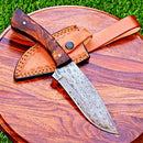 The Texan Knives Damascus Steel Hunting Knife – 10" with Rosewood Handle and Leather Sheath is displayed on a round wooden board, with green grass in the background.