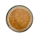 A top-down view of SALTOPIA Infused Sea Salts' Saltopia Caramel Sugar: DATE NIGHT 16oz, a clear glass jar filled with coarse, light brown caramel sugar crystals, ideal for gourmet baking, isolated on a white background.
