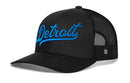 The Haka Hat Detroit Blue Script Trucker Hat is a black Michigan snapback featuring "Detroit" embroidered in blue script on the front, a curved brim, and a breathable black mesh back.