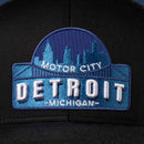 The Haka Hat Detroit Motor City Trucker Hat is a black cityscape snapback featuring blue and white Detroit skyline embroidery with "Motor City," "Detroit," and "Michigan" text.