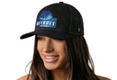 A woman with long brown hair smiles while wearing the Haka Hat Detroit Motor City Trucker Hat, a black cityscape snapback from Haka Hat, featuring a blue "Motor City Detroit Michigan" patch against a white background.
