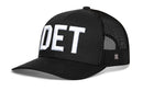 The Haka Hat Detroit White Block Trucker Hat by Haka Hat features a solid front, black mesh back, and bold white DET embroidery—perfect as a black Michigan snapback.